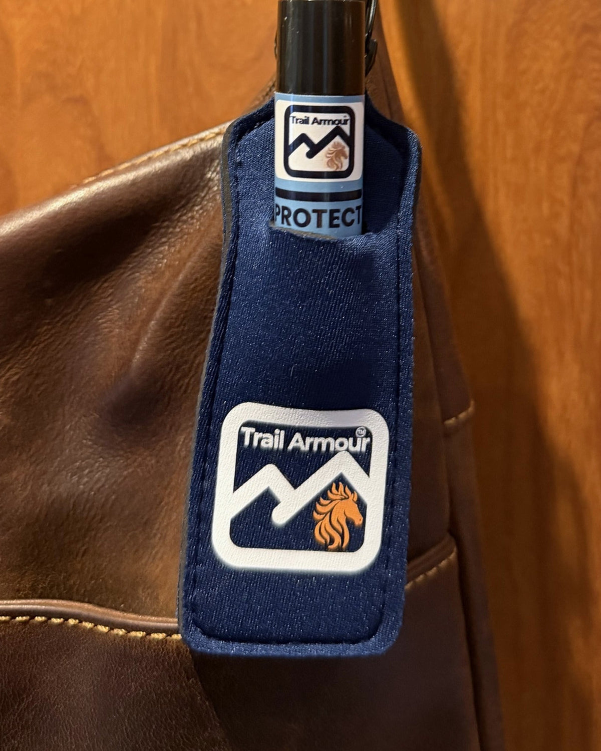 Trail Armour PROTECT lip balm tube sitting in a navy neoprene holder clipped to a bag