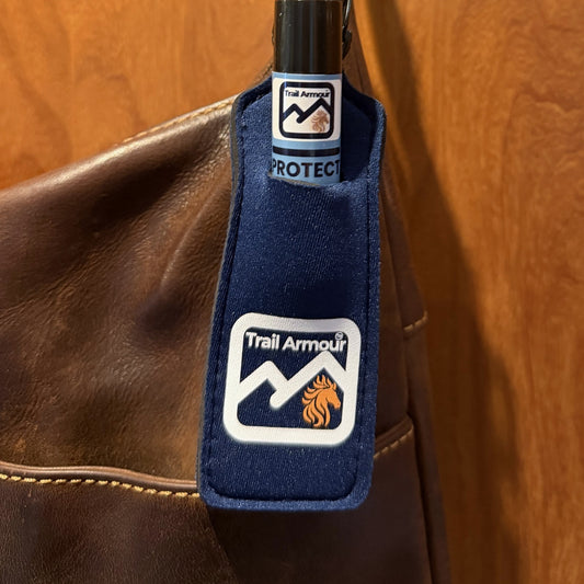 Trail Armour PROTECT lip balm tube sitting in a navy neoprene holder clipped to a bag
