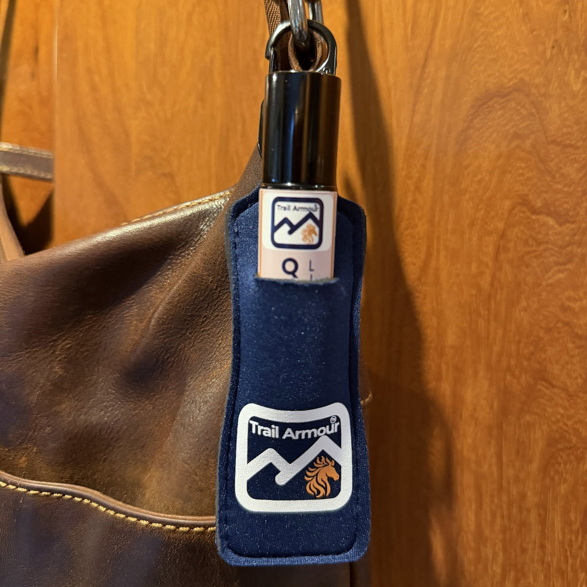 Trail Armour QUENCH lip serum roller sitting in a navy neoprene Trail Armour holder clipped to a bag