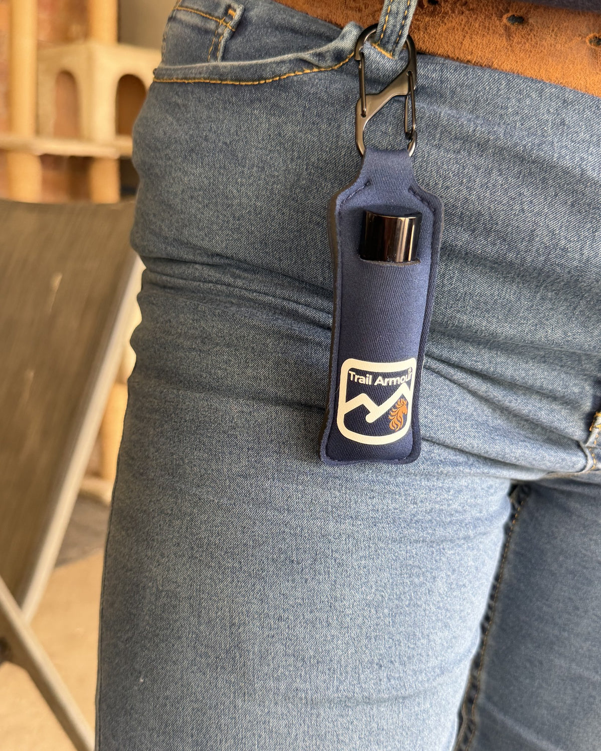 Navy neoprene Trail Armour lip balm holder clipped to a belt loop on jeans, holding a lip balm tube