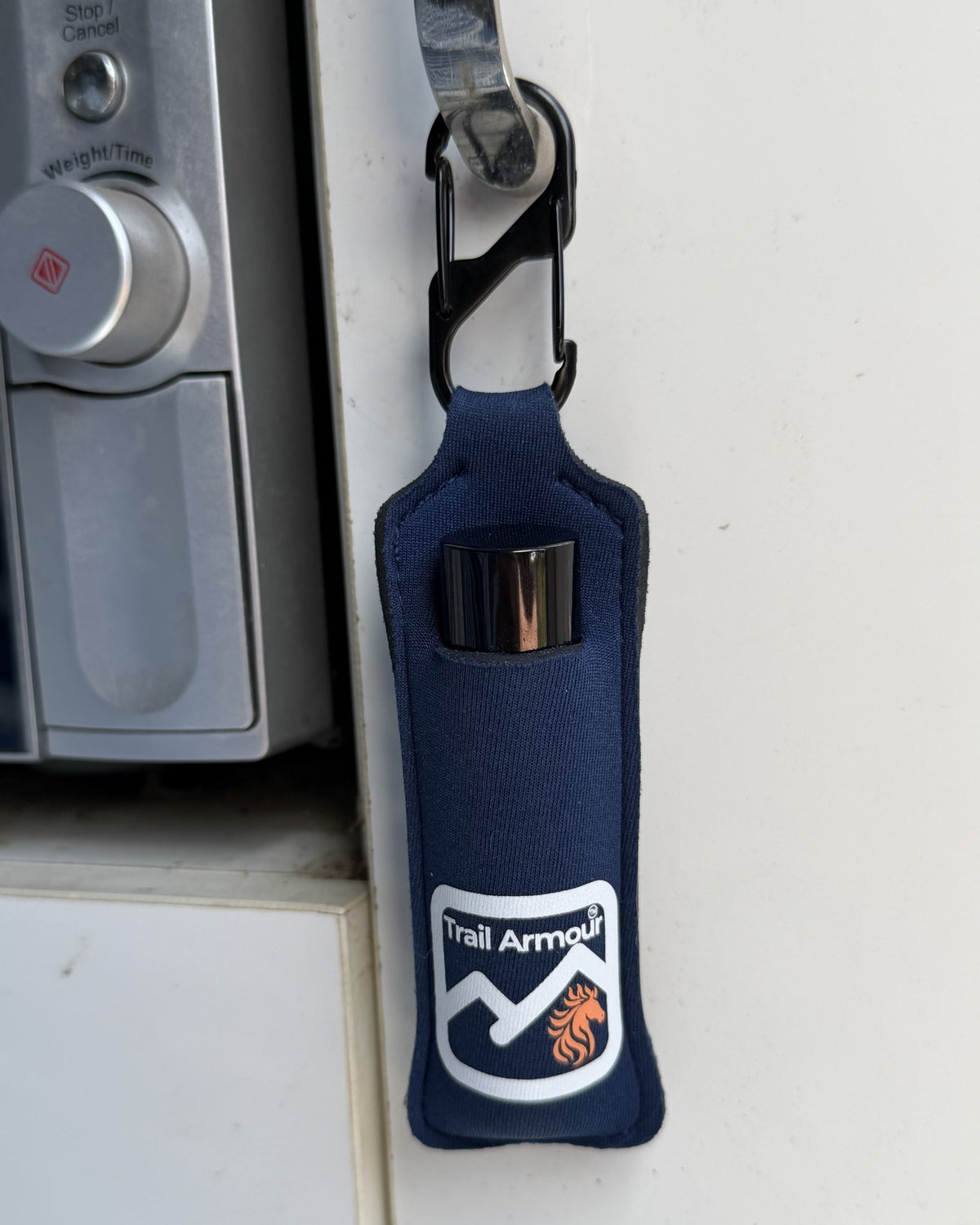 Navy neoprene Trail Armour lip balm holder holding a lip balm tube, resting on a kitchen bench