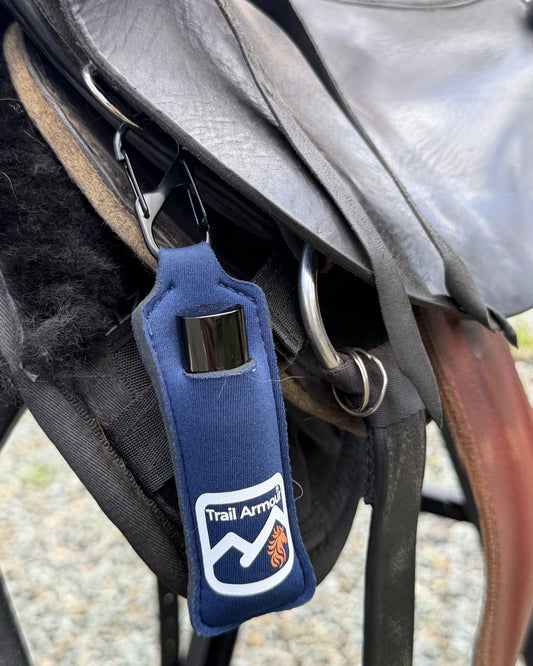 Navy neoprene Trail Armour lip balm holder clipped to a saddle, with a lip balm tube sitting in the front slot