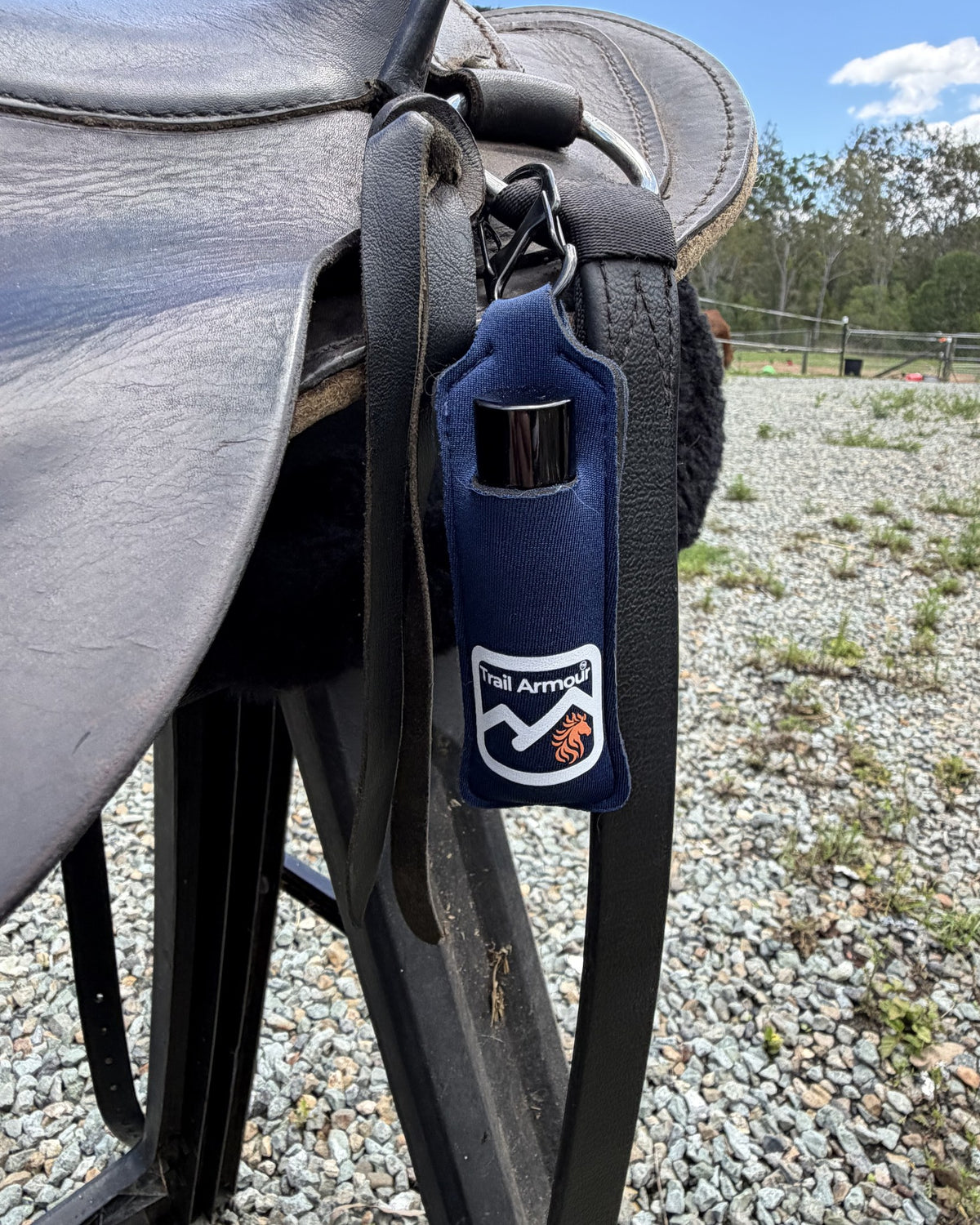 Navy neoprene Trail Armour lip balm holder clipped to a saddle on a rack, with bushland and blue sky behind